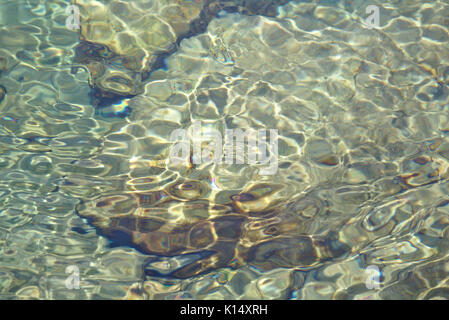 Acqua poco profonda su fondo roccioso con riflessioni e piccole onde increspata Foto Stock