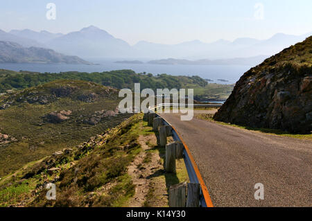 Single-lane road in montagna con il lago in background Foto Stock