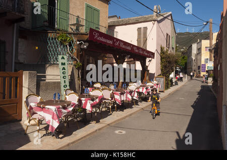 Francia, Corsica, Cap Corse, Centuri, scena di strada con outdoor cafe e il ciclista Foto Stock