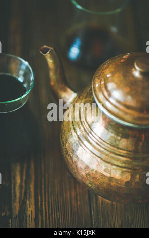 Oriental Medio Orientale rame vintage hummered teiere e tè nero in tradizionale tulip bicchieri su legno rustico sfondo, il fuoco selettivo ver Foto Stock
