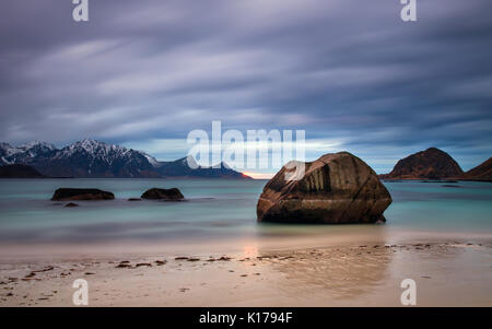 Roccia sulla spiaggia Haukland con montagne innevate sullo sfondo, Lofoten Foto Stock