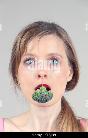 Giovane donna azienda broccoli dentro la sua bocca Foto Stock