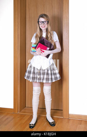 Ragazza giovane indossano uniformi scolastiche in piedi presso la porta prima di uscire per la scuola Foto Stock