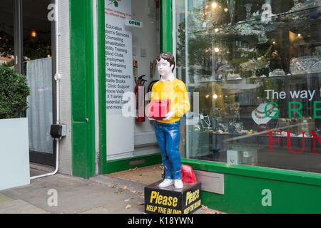 Si prega di aiutare i non vedenti cassetta di raccolta e statua al di fuori di prevenzione della cecità la società guarda di nuovo Shop su Kensington High Street, Londra, Regno Unito Foto Stock