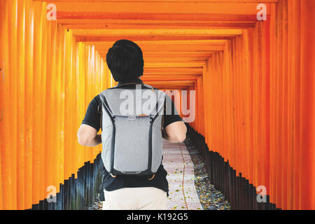 Asian uomo viaggiatori con zaino in piedi alla Red Gate dei tori a Fushimi Inari Shrine in Kyoto, Giappone. Foto Stock