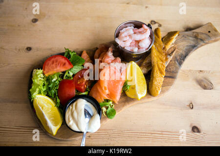 Piatto di frutti di mare su di un tagliere di legno e un tavolo di legno, gamberi, sgombro, salmone affumicato, insalata Foto Stock
