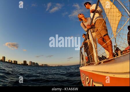 Attraente giovane coppia su una barca a vela in catamarano durante la crociera al tramonto sull'Oceano Atlantico fuori ft. Lauderdale, Florida, USA, scattata con lenti fisheye. Foto Stock