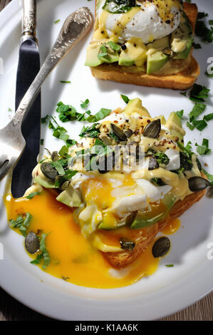 Uova Benedict su pane tostato con salsa olandese, fette di avocado Foto Stock