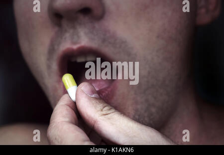 Close up uomo prendendo pillola medicina. Il giovane uomo messo in bocca pillola giallo isolato su sfondo blu. Foto Stock