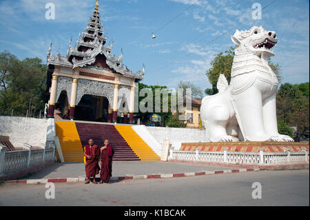 Due monaci buddisti posano per una fotografia ai piedi della scalinata che conduce al Mandalay Hill Myanmar davanti a un enorme statua Chinte Foto Stock