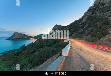 La Serpentina in montagna con la traccia di luce dal passaggio di un auto in twilight su uno sfondo di montagne, la Capezzagna e al mare. Foto Stock