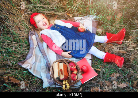 Bambina giacente in erba su un plaid con un cestino di frutta nella giornata d'autunno. Foto Stock