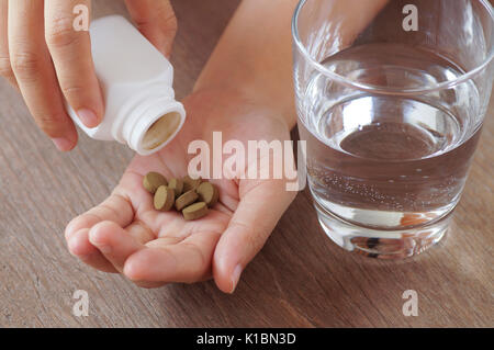 Medicina di erbe in pillole sulla mano di Palm con il vetro di acqua Foto Stock