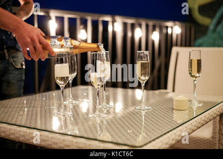 Mano d'uomo versa dello Champagne dal flacone in wineglasses sul tavolo. Foto Stock