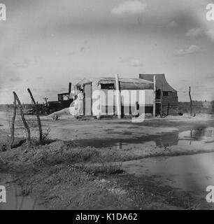 L'uomo entra in una grande tenda ad un accampamento migratori con vari edifici e una linea di abbigliamento, circondato da pozze di acqua, california, 1936. dalla biblioteca pubblica di new york. Foto Stock