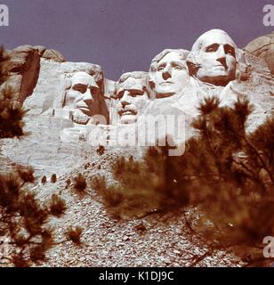 Una fotografia del monte Rushmore, presi da un angolo basso, vista è parzialmente ostruito da rami di albero, in Black Hills in Keystone, South Dakota, 1975. Foto Stock