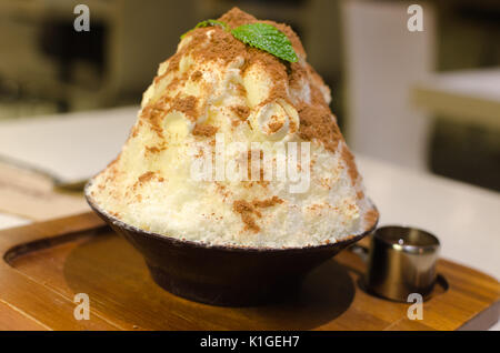 Ghiaccio trasparente Spining racchiudono il latte e rabboccato con il cacao in polvere in un recipiente con nero dessert asiatici. Foto Stock
