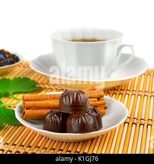 Tazza da tè, cioccolatini e cannella sul tappetino di bambù su sfondo bianco Foto Stock