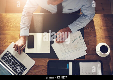 Consulente finanziario seduto alla sua scrivania in un ufficio la revisione di documenti e lavorare online con un computer portatile Foto Stock