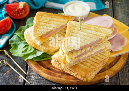 Premuto e tostato double sandwich con prosciutto e formaggio, servita con foglie di lattuga su una cucina un tavolo di legno. Foto Stock