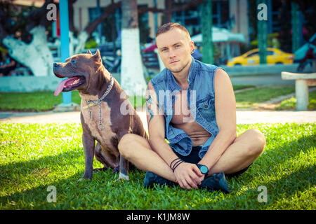 Happy amici uomo e cane american pit bull terrier seduto sull'erba in posizione di parcheggio Foto Stock