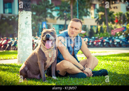 Happy amici uomo e cane american pit bull terrier seduto sull'erba in posizione di parcheggio Foto Stock