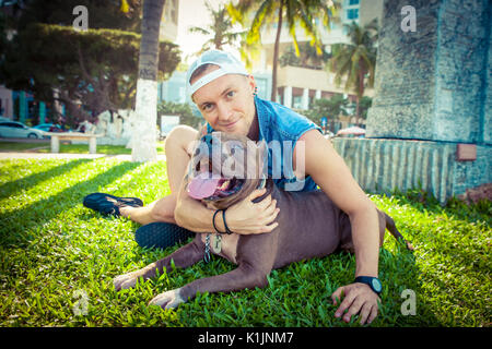 Uomo e cane american pit bull terrier di relax presso il parco abbracciando e abbracciando Foto Stock