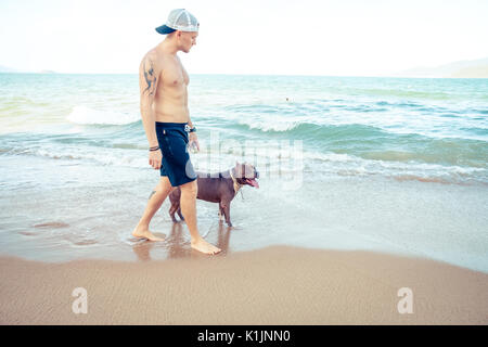 Giovane Uomo con cane american pit bull terrier di camminare sulla spiaggia tropicale Foto Stock