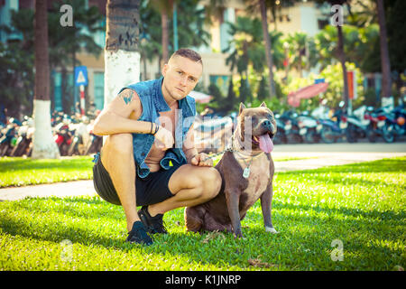 Happy amici uomo e cane american pit bull terrier seduto sull'erba in posizione di parcheggio Foto Stock