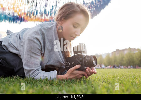 Bella femmina caucasica utilizzando una pellicola fotocamera. Viaggiare donna prendendo foto sulla fotocamera vintage all'aperto in estate Foto Stock