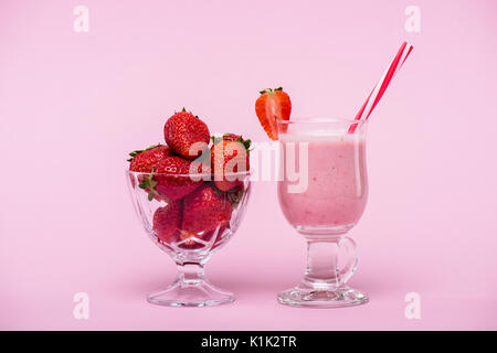 Delizioso frullato fragole in vetro con paglia e fragole fresche in un recipiente isolato in rosa Foto Stock