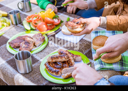 Vista ravvicinata di mani umane e il cibo gustoso sul tavolo, famiglia di mangiare al picnic Foto Stock