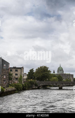 Galway, Irlanda - 3 Agosto 2017: grigio impetuoso fiume Corrib con Bridge Street Bridge e la cupola della Cattedrale di Galway che sovrasta il resto sotto egli Foto Stock