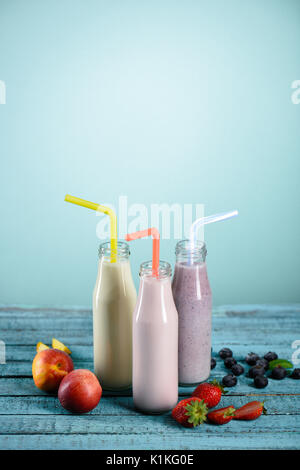 In casa fruttato frappè in bottiglie di vetro con cannucce e ingredienti freschi sul piano portapaziente su blu Foto Stock