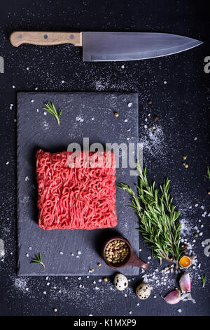 Rosso di manzo crudo, con gli ingredienti della cucina, servita su una pietra bordo, coltello da cucina. Vista superiore, copia dello spazio. Foto Stock