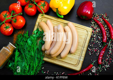 Salsicce sul bordo di taglio disposti con le verdure e il verde su un tavolo di legno per uno spuntino in campagna. Pomodoro, il bianco e il rosso dei peperoni e sp Foto Stock