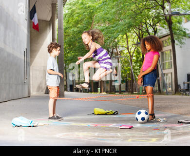 Ragazzo salta con gli amici dopo la scuola su manto elastico giocando yoki gioco Foto Stock