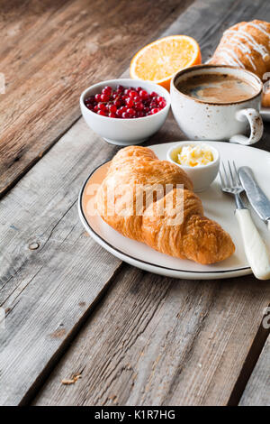 Croissant fresco, una tazza di caffè, arancio, bacche su tavola in legno rustico. Angolo di visione e copia di spazio. Prima colazione continentale Foto Stock