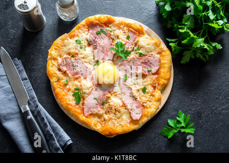 Pizza Carbonara sulla pietra nera dello sfondo. Pizza italiana Carbonara con pancetta, uova e formaggio vicino. Foto Stock