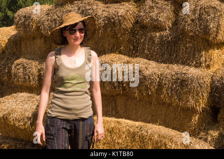 Bella donna con cappello appoggiandosi a balle di paglia in una giornata di sole. Foto Stock