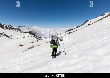 Una femmina di escursionista attraversa un snowfield sopra le nuvole sul modo di Monarch laghi in re minerale. Foto Stock