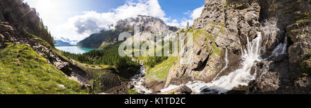 Vista panoramica di un torrent stream sorgente e del lago in una verde vallata nelle Alpi Svizzere montagne nella soleggiata estate, perfetto per banner Foto Stock