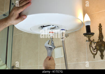 Uomo con le mani una chiave la riparazione di tubi per acqua calda e fredda su una caldaia in un bagno Foto Stock