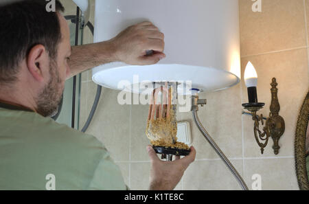 Uomo di prendere un vecchio calorifero di acqua con il deposito di calcare da una caldaia in un bagno Foto Stock