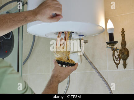 Plumber tenendo fuori un vecchio calorifero di acqua con il deposito di calcare da una caldaia in un bagno Foto Stock