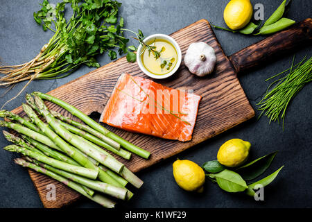 Ingredienti per la cottura. Materie filetto di salmone, gli asparagi e le erbe sul pannello di legno. Per la cottura di alimenti con sfondo spazio copia. Vista superiore Foto Stock