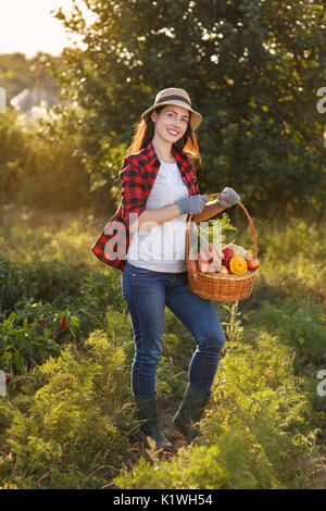 Il Giardiniere di fresco con verdure raccolte in giardino con sole. Donna felice l'agricoltore che detiene il cestello con il raccolto. Il giardinaggio, l'agricoltura, l'autunno harves Foto Stock