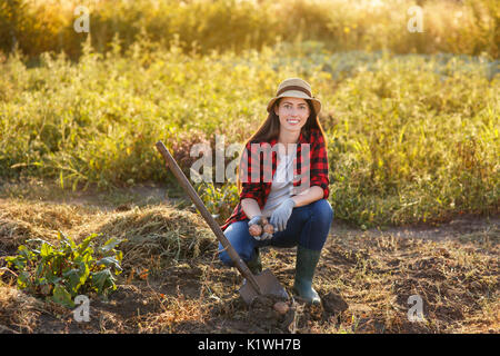 Felice giovane donna giardiniere con patate in giardino. Giovane agricoltore la raccolta di patate. Il giardinaggio e agricoltura, raccolto autunnale concept Foto Stock