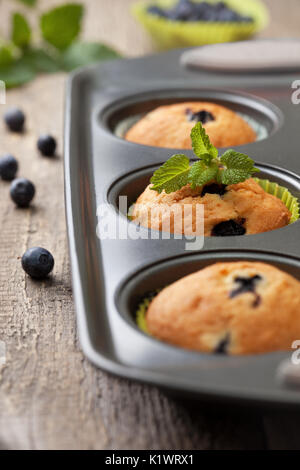Muffin con i mirtilli in una teglia sul vecchio sfondo di legno Foto Stock