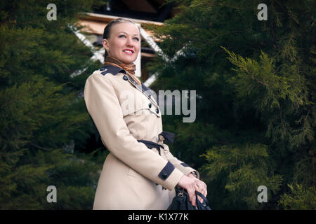 Felice ragazza nel cappotti a ulybvaetsja tra il verde di alberi Foto Stock